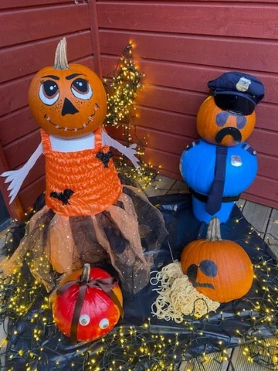 En pumpa-dam med pliriga ögon och orange klänning står bredvid en polis gjord av en pumpa, med uniform, slips och hatt.