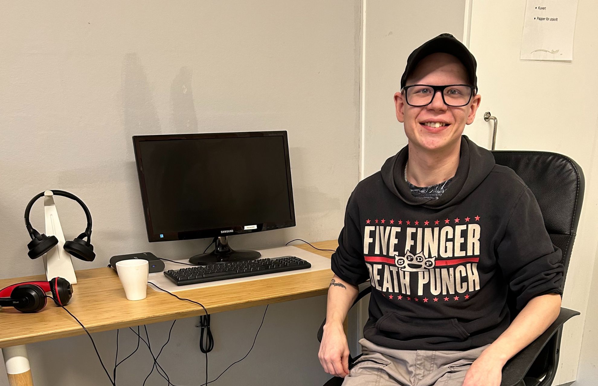 Hampus sitter i en stol bredvid en datorskärm och ler.