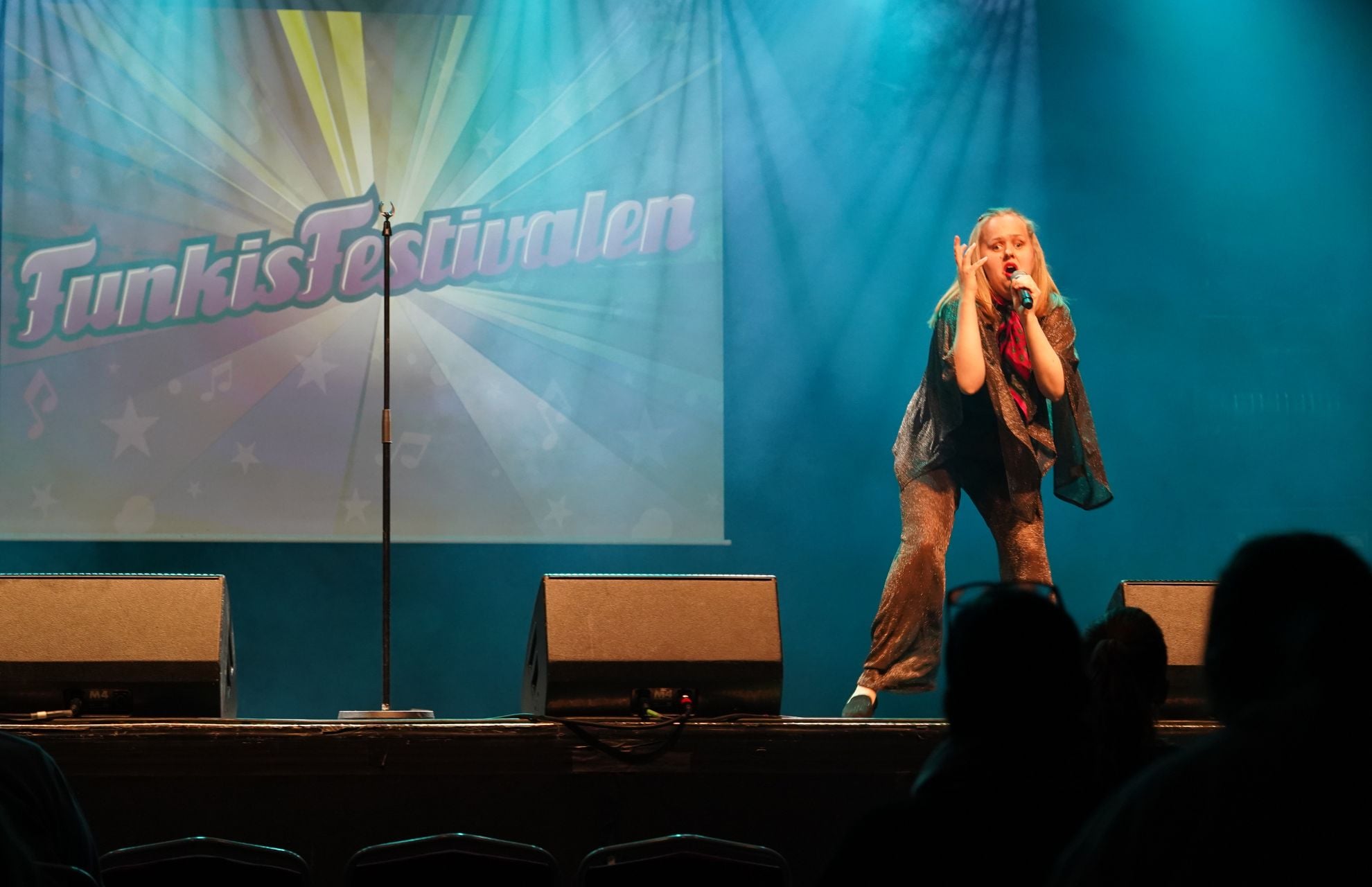 En deltagare sjunger på scen framför backdrop där det står Funkisfestivalen
